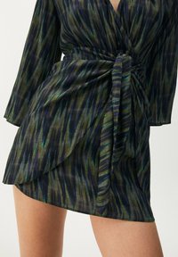 Kort klänning i lätt material med ett flerfärgat mönster av vertikala randiga i grönt, blått och svart. Har en knytning i midjan.