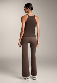 Rjav rebrast top s tank skodelico v kombinaciji z rjavimi širokimi hlačami, ki se ponašajo z gladko teksturo in prilegajočim dizajnom, prikazan od zadaj.