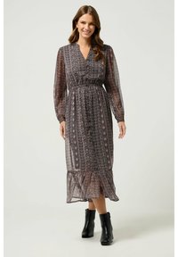 Vestido largo y fluido de tela transparente con patrones florales oscuros, cintura elástica, escote en V y mangas largas; combinado con botas negras hasta el tobillo.