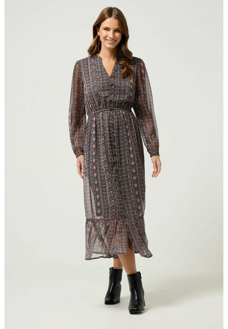 Vestido largo y fluido de tela transparente con patrones florales oscuros, cintura elástica, escote en V y mangas largas; combinado con botas negras hasta el tobillo.