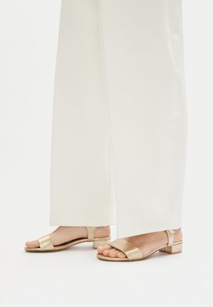 Goldfarbene metallic Sandalen mit einem niedrigen Blockabsatz, die zwei breite Riemen über den Zehen und einen Knöchelriemen für einen sicheren Sitz aufweisen.