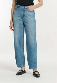 Jasnoniebieskie jeansy z wysokim stanem o prostym kroju, z paskami do paska, kieszeniami z przodu i surowym wykończeniem. Włożone z czarnymi balerinami.