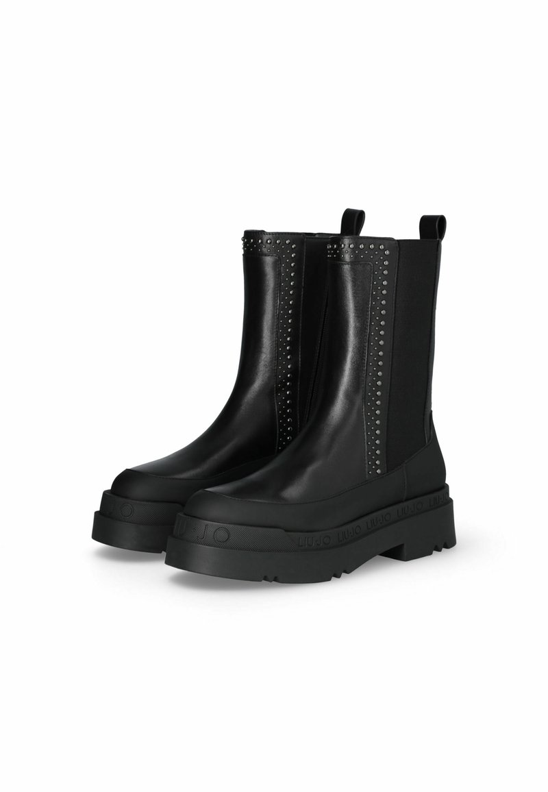 Bottines noires en cuir avec semelles en caoutchouc épaisses, côtés élastiques et accents cloutés le long des coutures. Comprend des languettes pour un enfilage facile.