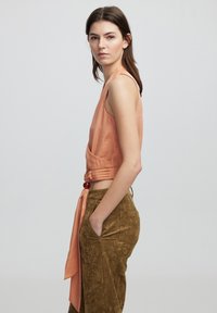 Top senza maniche color pesca con dettaglio vita annodata, abbinato a pantaloni texturizzati verde oliva con tasche laterali.