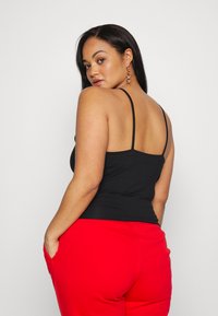 Top aderente nero con spalline sottili, abbinato a pantaloni della tuta rossi. Il top ha un design semplice e una texture liscia.