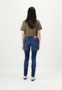 Smal jeans i en mørk blå vask med baklommer og en brun lærlabel i midjen. Kombinert med en nøytral t-skjorte.