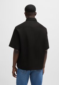 Zwart shirt met korte mouwen en een kraag, met een gladde textuur en een rechte zoom, gedragen met blauwe spijkerbroek.