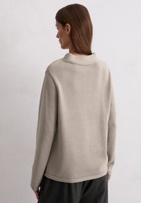 Beige Strickpullover mit hohem Kragen und gerippter Textur, der eine gerade Passform hat und dezente Nahtdetails an den Schultern aufweist.