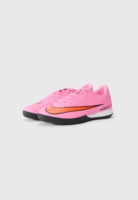 Des chaussures de sport roses avec une texture lisse, présentant un swoosh orange, une semelle noire et des lacets plats. La marque est visible au niveau du talon.