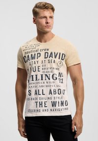 Light beige t-shirt featuring dark blue text and nautical-themed graphics, short sleeves, and a crew neckline. Text expresses sailing themes.