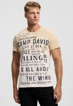 Hellbeiges T-Shirt mit dunkelblauem Text und nautischen Grafiken, kurzen Ärmeln und Rundhalsausschnitt. Der Text thematisiert das Segeln.