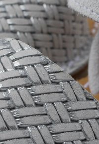 Grijze geweven slippers met een gestructureerd oppervlak, voorzien van glanzende accenten. Gedetailleerd vlechtpatroon over de zool, van zacht materiaal.