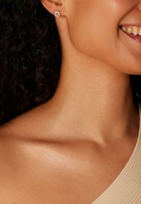 Bloemvormige oorbel met rozenkleurige accentstenen en een centrale witte edelsteen, gezet in een zilverkleurige montuur, gedragen door een model met krullend haar.