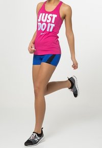 Top rosa di Nike con testo bianco "JUST DO IT", abbinato a pantaloni corti blu con dettagli neri e scarpe da ginnastica nere.