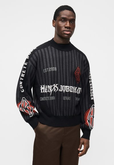 Knitted sweater in black with vertical stripes. Features bold logos and text in white and red. Fitted ribbed collar and cuffs.
