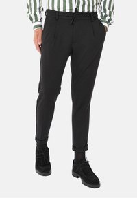 Czarne spodnie zwężane z ściągaczem w talii, z przednimi zakładkami. Połączone z czarnymi butami, prezentującymi gładką fakturę i uniwersalny design.