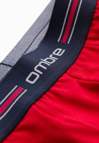 Röd tyg med elastisk midja som har en blå design och vit text "ombre." Inkluderar smala röda och vita ränder. Slät textur.