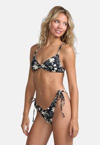 Bikini noir avec motif floral blanc, comprenant un haut triangle et un bas à nouer sur les côtés, fabriqué dans un tissu lisse et extensible.