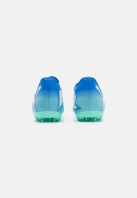 Botas de fútbol en degradado azul con una parte superior texturizada, que presentan un logo blanco y una suela verde. Suela con tacos para tracción en superficies de hierba.
