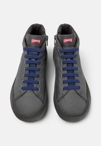 Zapatillas gris alto con cordones azul marino y logo en rojo de "Camper" en la lengüeta, vistas desde arriba sobre un fondo blanco.