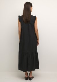 Black sleeveless maxi dress with ruffled shoulder accents, tiered hem, and smooth fabric texture. Back view shows draped shape and length.