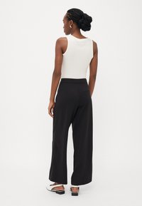 Hvit ribbet tanktop kombinert med svarte vide bukser, som har en baklomme og en glatt tekstur. Svarte og hvite sandaler.
