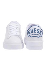 Sneakers bianchi in pelle con punta rotonda, suola piatta bianca e logo blu "GUESS LOS ANGELES" sulla linguetta del tallone. Design con lacci frontali.