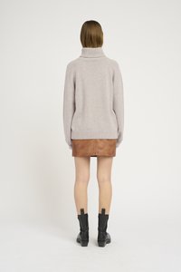 Maglione grigio chiaro con colletto alto, abbinato a una mini gonna di pelle marrone e stivali neri alla caviglia. Design semplice, texture morbida.