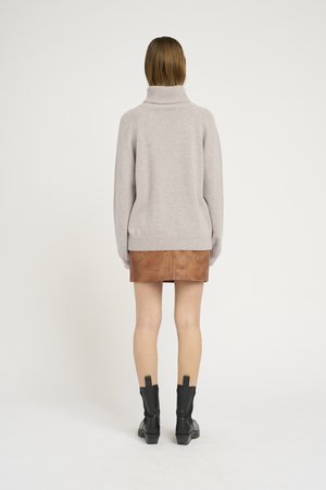 Maglione grigio chiaro con colletto alto, abbinato a una mini gonna di pelle marrone e stivali neri alla caviglia. Design semplice, texture morbida.