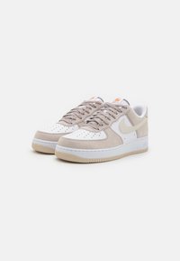 Beige suède en witte leren sneakers met geperforeerde neus, ronde veters en een lichtbruine rubberen zool met gestructureerde details.