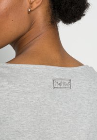 Top grigio a costine con scollatura ampia e un piccolo etichetta del marchio cucita sul retro. Il materiale sembra morbido con una texture liscia.