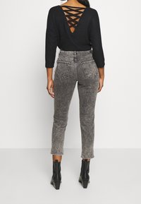 Camisa negra de manga larga con espalda en forma de V y detalles entrecruzados, combinada con jeans de tiro alto en gris desgastado y botas de tobillo negras.