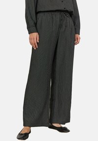 Pantaloni neri a gamba larga con strisce verticali bianche, dotati di vita elasticizzata e lacci. Orlo affusolato con una finitura morbida e testurizzata.