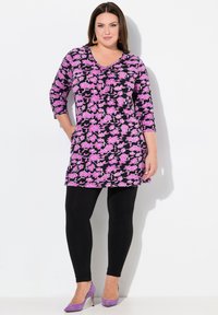 Blommig tunika med rosa och lila blommor på svart bakgrund, tre fjärdedelars ärmar, matchad med svarta leggings och lila klackar.