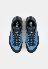 Blue climbing shoes with black rubber trim, featuring a textured surface and reinforced toe. Laces are blue with branded accents in white.