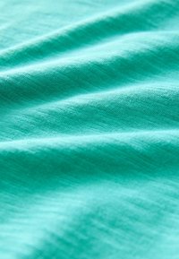 Türkisfarbener Stoff mit weicher Textur, der sanfte Falten und ein dezentes, gleichmäßiges Webmuster aufweist. Glattes und leichtes Material.