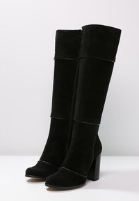 Svarta knähöga boots i mocka med en kraftig klack, med en dragkedja fram och kontrasterande läderdetaljer längs den övre sömmen.