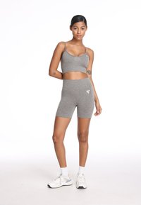 Szara sportowa kompleta składająca się z topu na ramiączkach i szortów z wysokim stanem. Materiał jest gładki, z subtelną teksturą; widoczny detal logo.