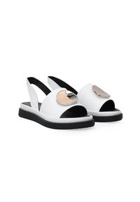 Weiße Rutschen-Sandalen mit offenem Zeh und Fersenriemen, die vorne mit einem großen silbernen runden Akzent und einer schwarzen Sohle ausgestattet sind.