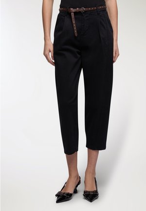 Pantaloni neri cropped con vita alta e cinturino, dotati di una superficie liscia e pieghe laterali. Abbinati a tacchi slingback neri in vernice con dettagli a fiocco.