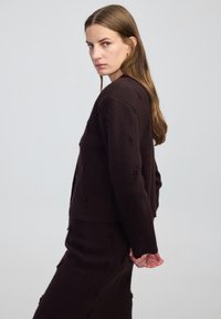 Bruine gebreide cardigan met textuurdetails, met een cropped ontwerp en lange mouwen, gecombineerd met een bijpassende rok.