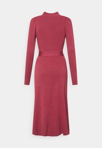 Robe à manches longues en tissu côtelé de couleur rose profond. Elle présente une taille cintrée avec une ceinture assortie et une jupe fluide légèrement évasée.