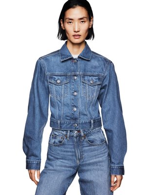 Femme portant une veste en jean bleue ajustée avec des poches poitrine boutonnées et un jean bleu taille haute sur fond blanc.
