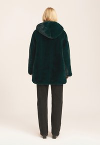 Dark green faux fur coat with a hood, featuring a soft texture, slightly oversized fit, and long sleeves, paired with black pants.