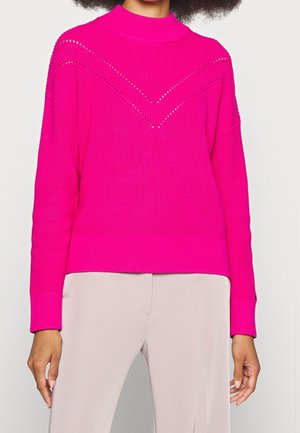 Pull en tricot fuchsia avec un col montant, présentant des motifs de points texturés et des découpes diagonales sur la poitrine. Manches longues.