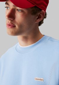 Γαλάζια μπλούζα με ριγωτό γιακά, με μικρή ετικέτα λογότυπου Calvin Klein σε κρέμα και κόκκινο μπροστά. Μαλακή υφή.