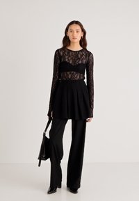 Μαύρο μακρυμάνικο τοπ από δαντέλα πάνω από στεντό μαύρο κορμάκι, συνδυασμένο με μαύρη πλισέ φούστα και καλοραμμένο μαύρο παντελόνι, συνοδευόμενο από μαύρη τσάντα.