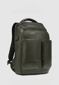 Olijfgroene leren rugzak met twee voorzakken met rits, een handvat aan de bovenkant, gevoerde achterkant en verstelbare riemen. Soepele textuur en strak ontwerp.