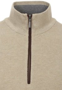 Beiger Strickpullover mit hohem Kragen, halbem Reißverschluss vorne und kontrastierender brauner Reißverschlussdetails. Weiche Textur, gerippter Stoff.