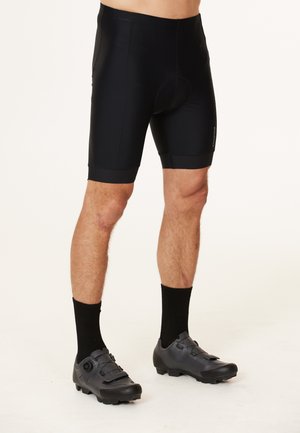 Shorts da ciclismo neri con un design aderente, texture liscia e un centro imbottito. Indossati con scarpe da ciclismo nere dotate di cinturini regolabili.